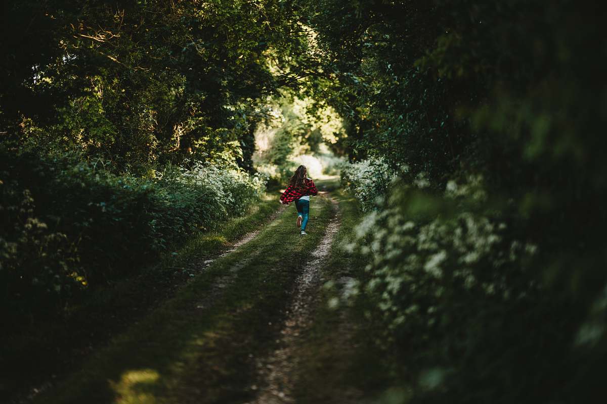 sports woman in red shirt and green pants walking on grass road between trees during daytime tree